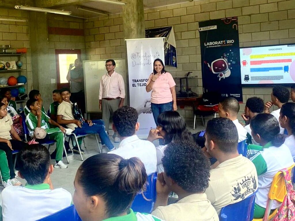 Taller de formación en un aula con estudiantes de colegio; una facilitadora habla frente al grupo durante una sesión sobre emociones.