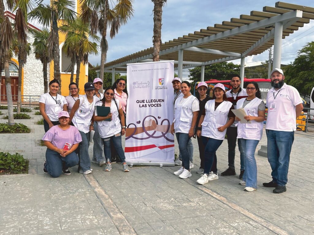 Equipo de Tejedores de Diversidad junto al pendón de la jornada «Que lleguen las voces», realizada con la Gobernación del Atlántico.