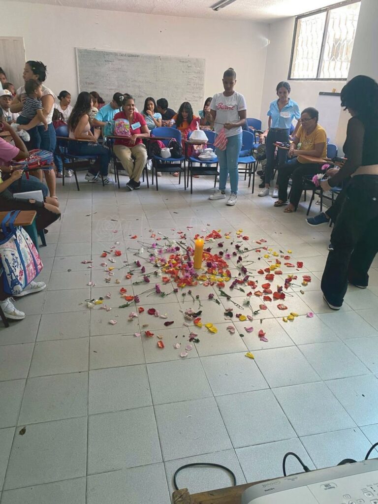 Participantes de un taller comunitario alrededor de un mandala de flores en el suelo.